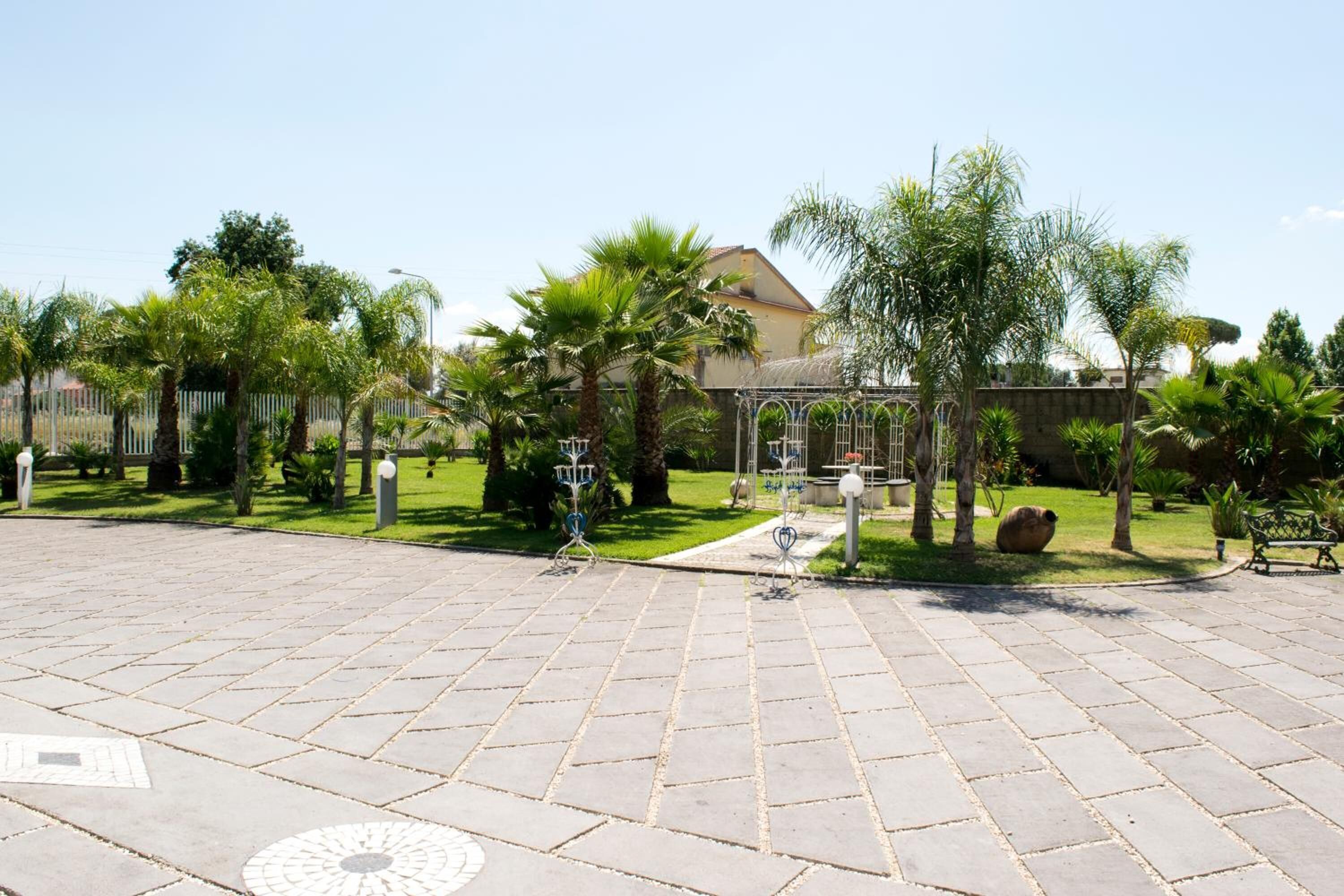 A paved courtyard with palm trees, a gazebo, and a pathway leading to a building.