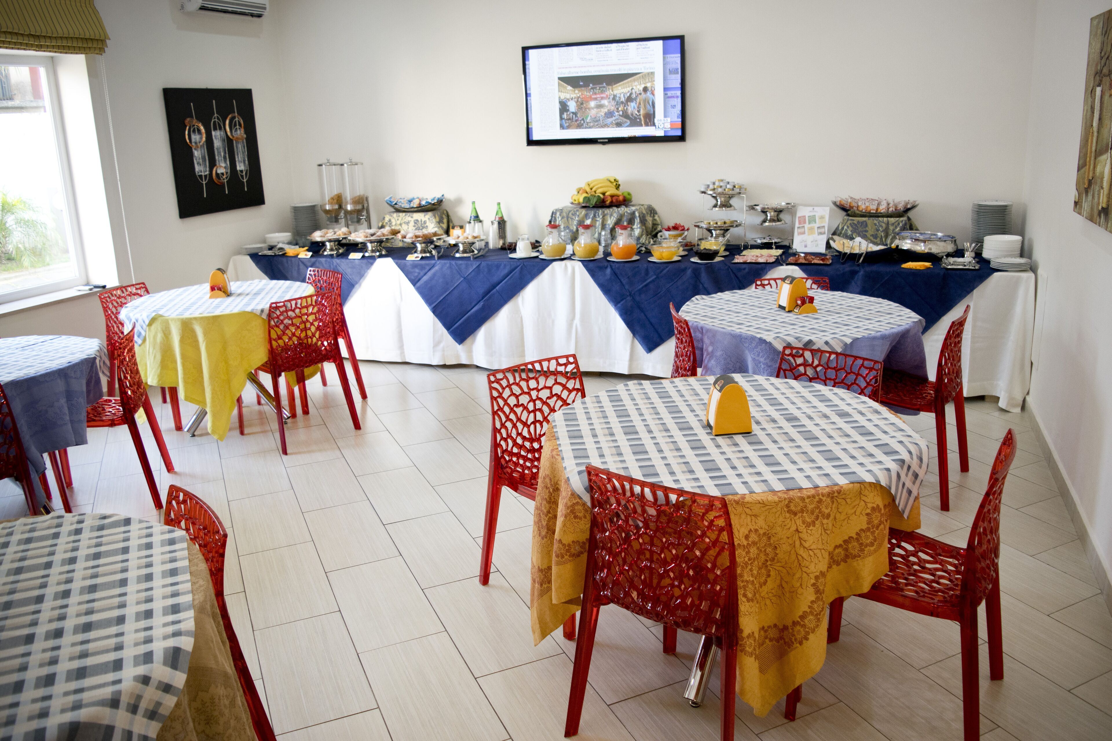 A dining area with multiple tables and chairs, a buffet setup, and a television on the wall.