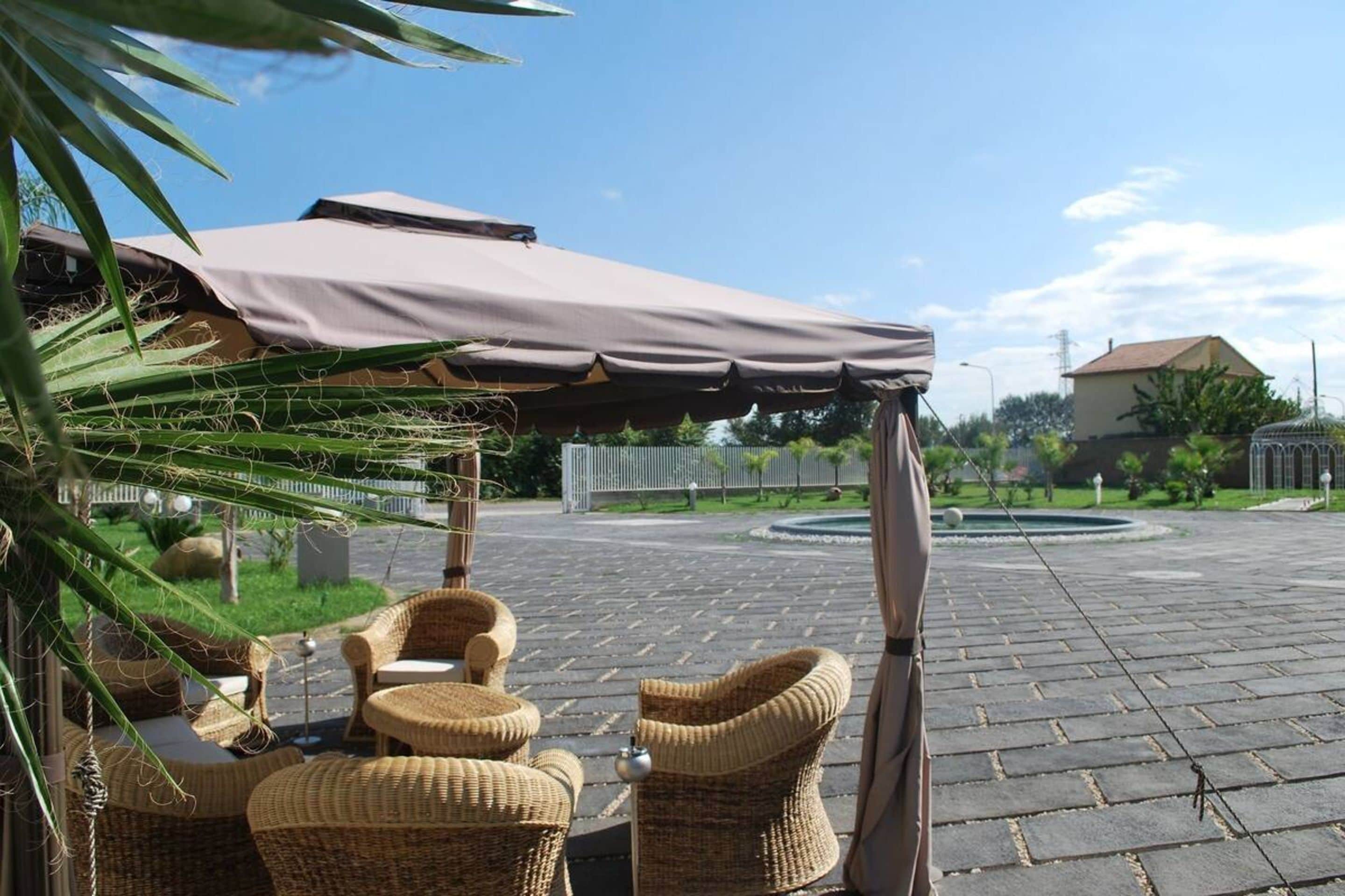An outdoor seating area with wicker furniture under a canopy, a paved courtyard, and a building in the background.