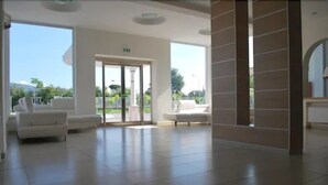 Un hall espacioso con un gran ventanal que da al exterior, sofás blancos y suelo de baldosas.