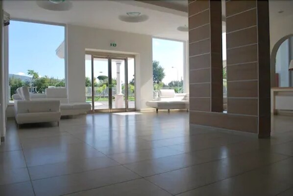Un hall espacioso con un gran ventanal que da al exterior, sofás blancos y suelo de baldosas.