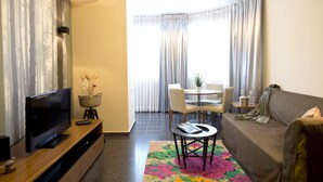 A modern living room with a flat-screen TV, a sofa, a dining table with chairs, and a colorful rug. - King George 83 Vacation apartments (Tel Aviv)