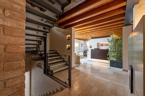 A modern interior with a staircase, wooden ceiling beams, and a kitchen area in the background.