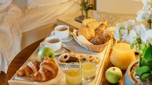 Una bandeja de desayuno bien preparada con croissants, una taza de café, jugo y una manzana verde sobre una mesa de madera en una habitación de hotel.