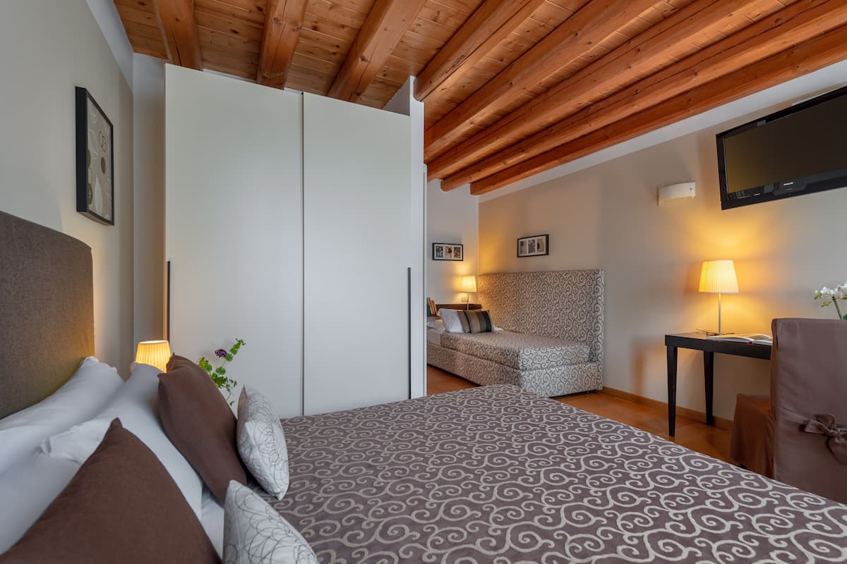 A bedroom with a bed, a sofa, a TV, and a desk with a lamp.