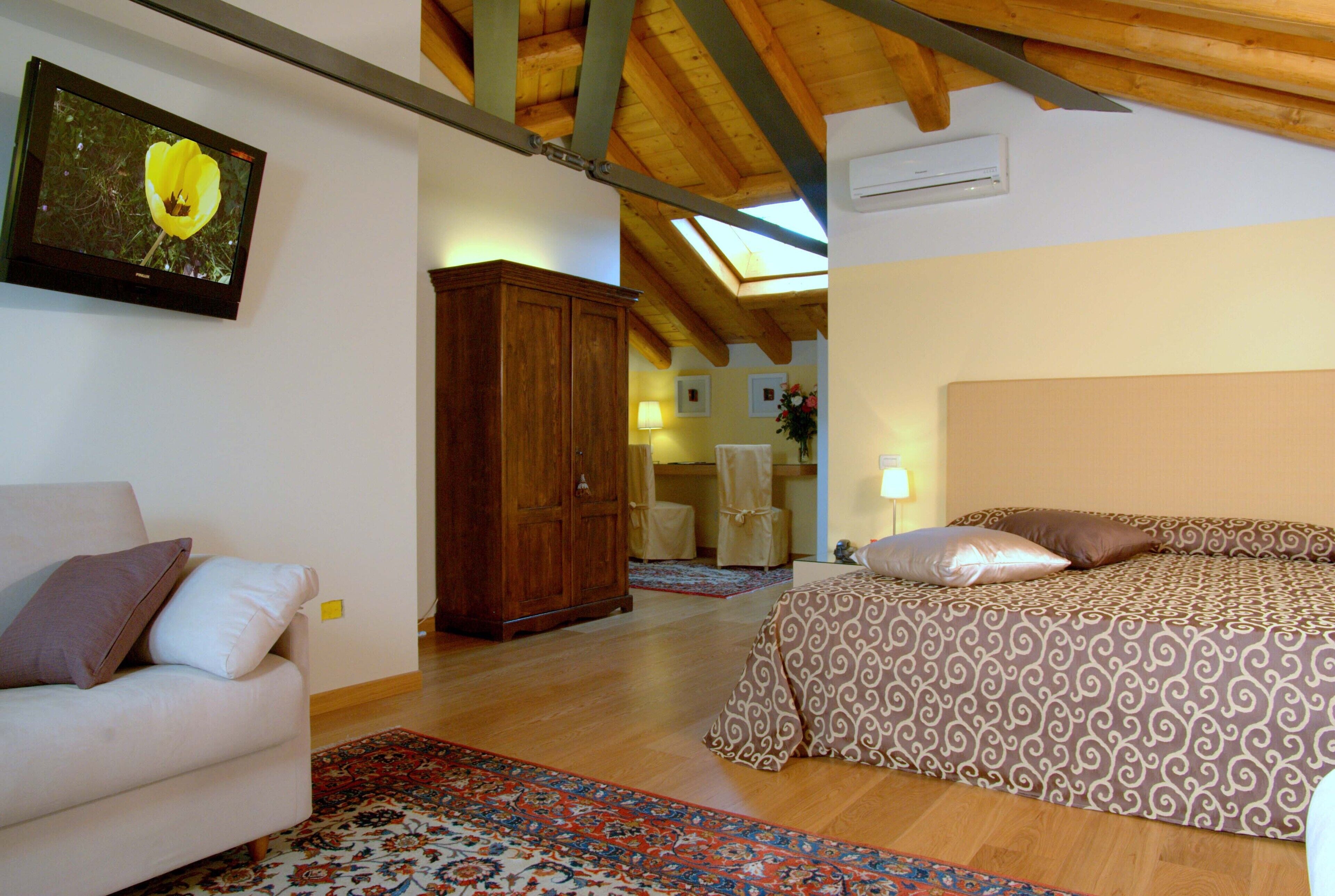 A bedroom with a bed, a sofa, a wooden wardrobe, and a television displaying a flower.