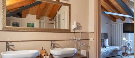 A bathroom with wooden beams, a large mirror, two sinks, and a small stool with towels.