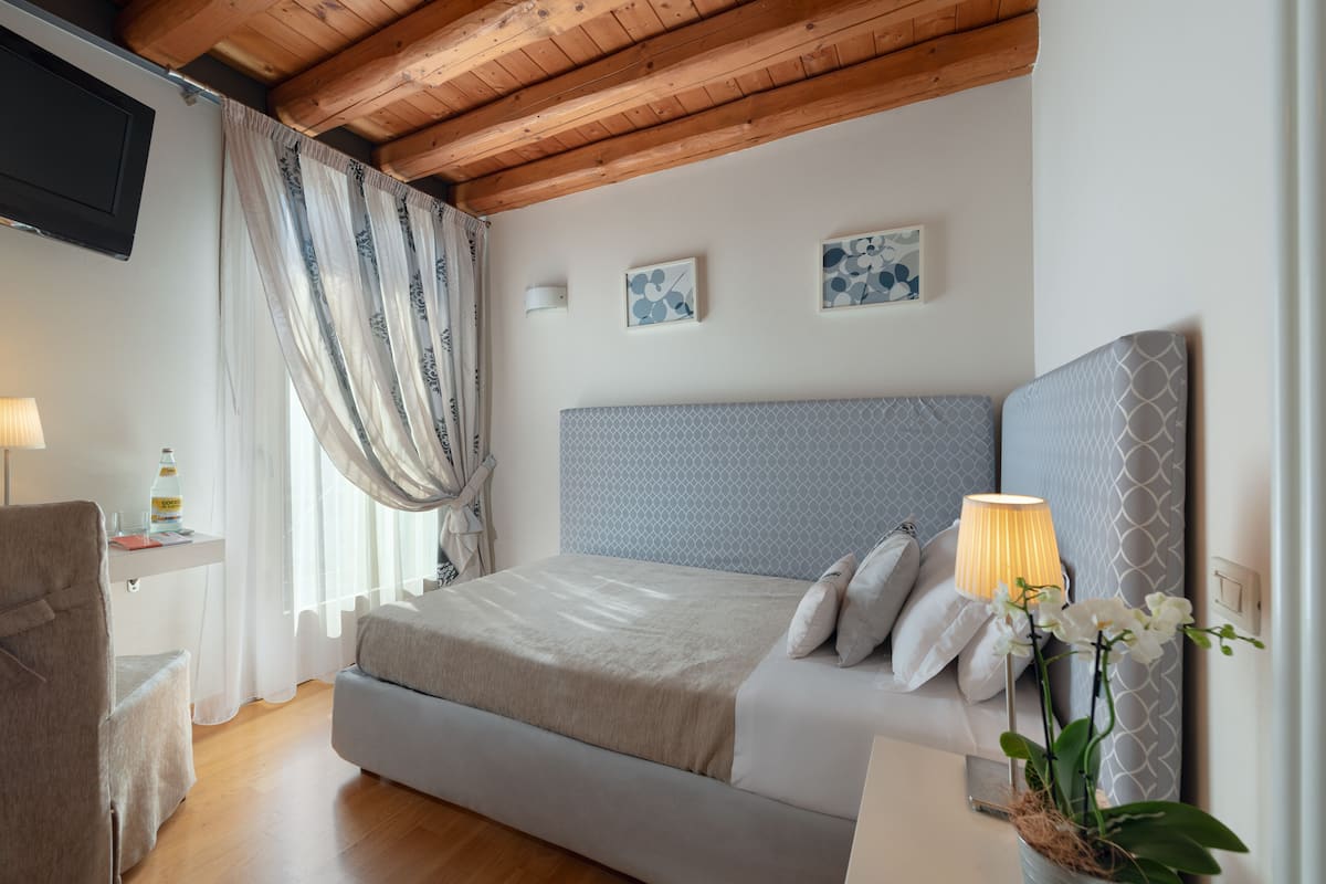 A bedroom with a bed, a bedside lamp, a chair, a desk, and a potted plant.