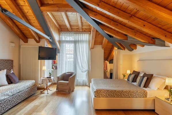 A bedroom with a wooden ceiling, a bed, a sofa, a chair, a TV, and a window with curtains.