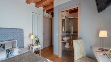 Habitación de hotel con cama, mesita de noche, lámpara y vista al baño.