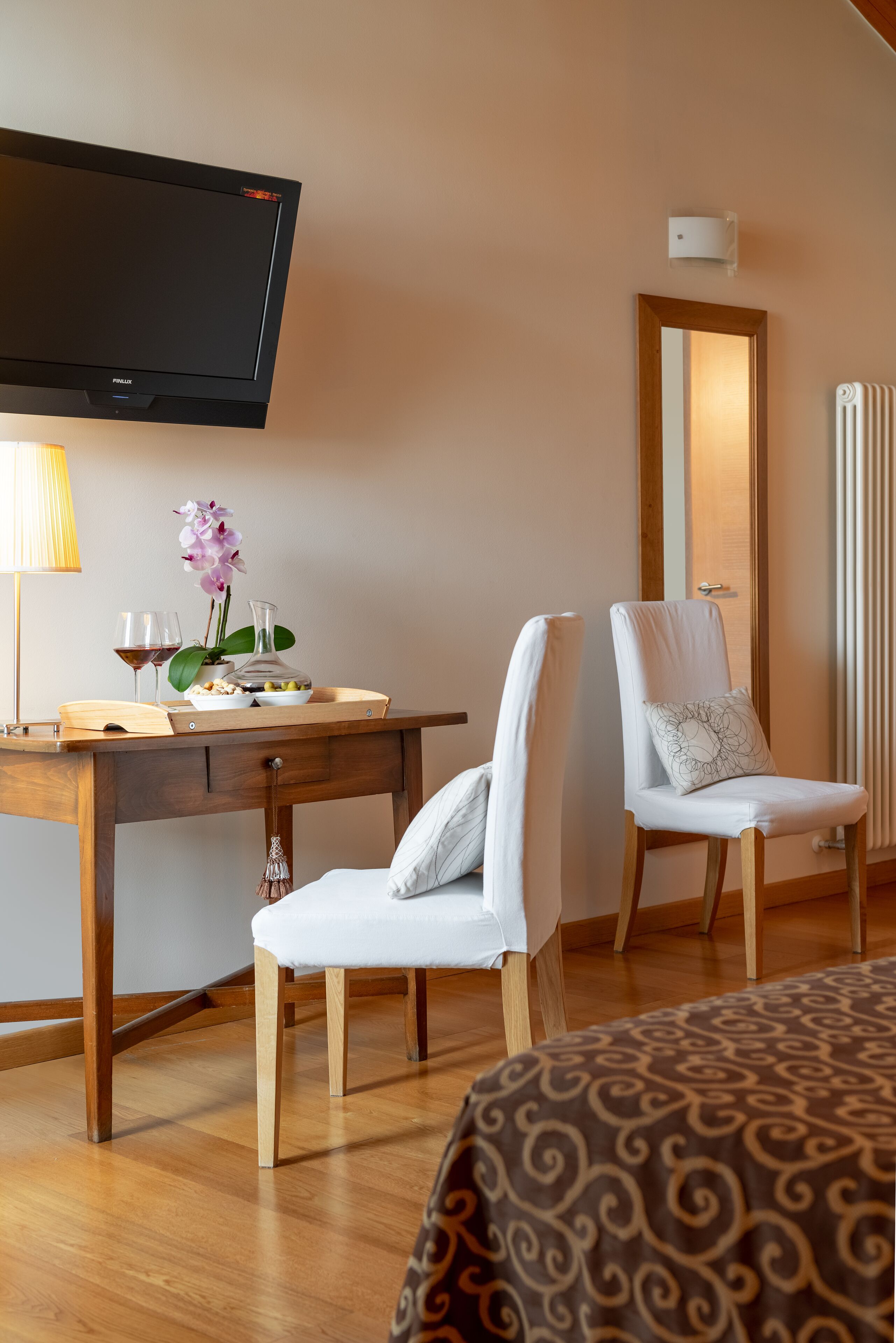 Ein Hotelzimmer mit einem Holztisch, einem Fernseher, einem Sessel, einem Bett und einem Spiegel.