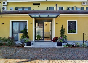 A yellow building with a modern entrance, potted plants, and a brick pathway.