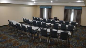 A conference room with a long table and chairs, carpeted floor, and curtains on the windows.