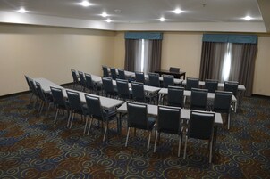 Un salón de conferencias con una larga mesa y sillas, piso alfombrado y cortinas en las ventanas.