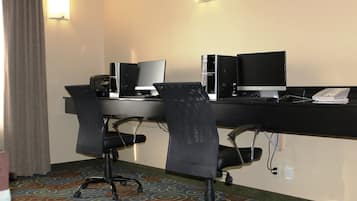 A hotel room with a desk, two chairs, a computer, a phone, and a lamp.