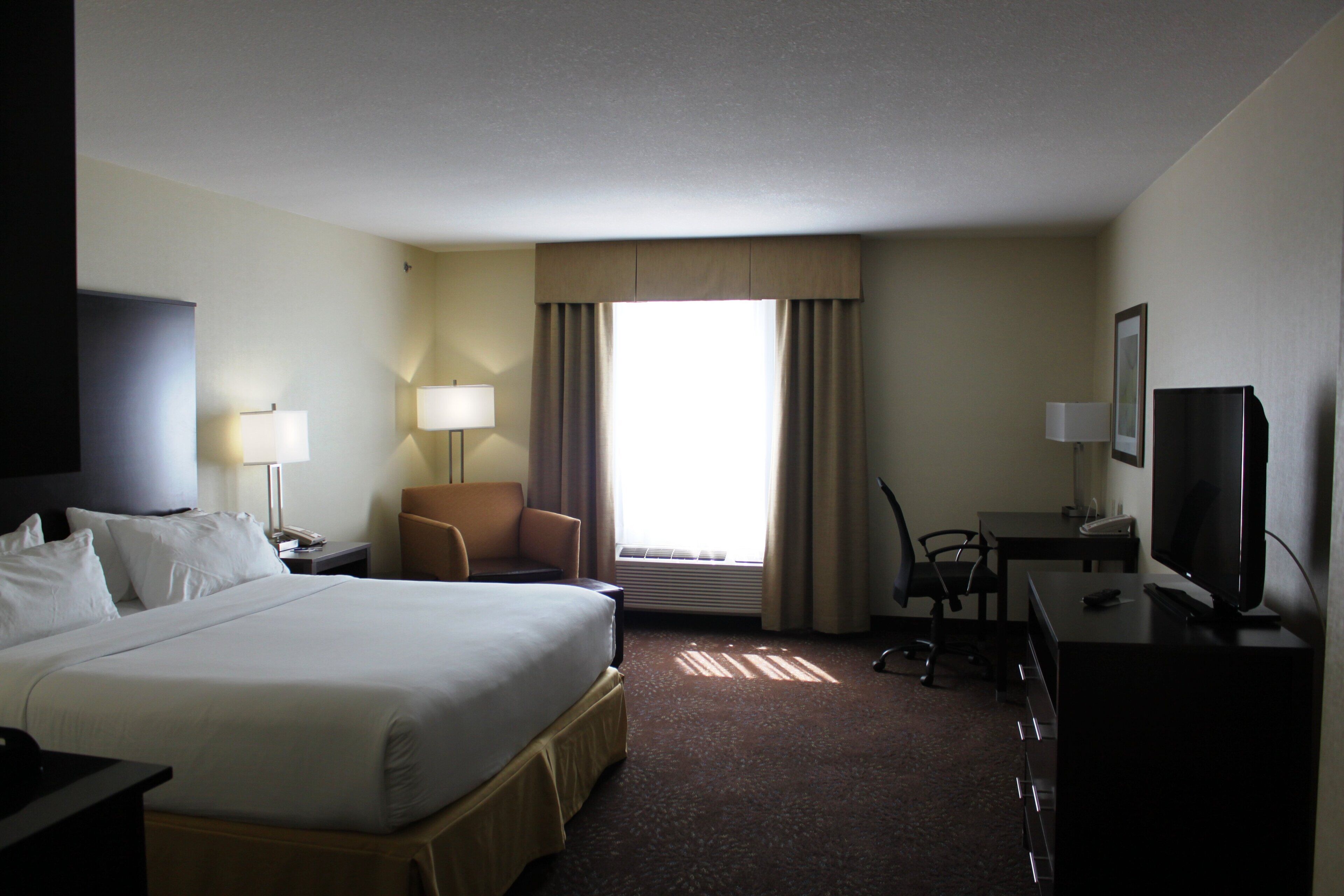 A hotel room with a large bed, a desk with a computer, a chair, and a television.