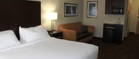 A hotel room with a large bed, a desk, a chair, a small kitchenette, and a microwave.