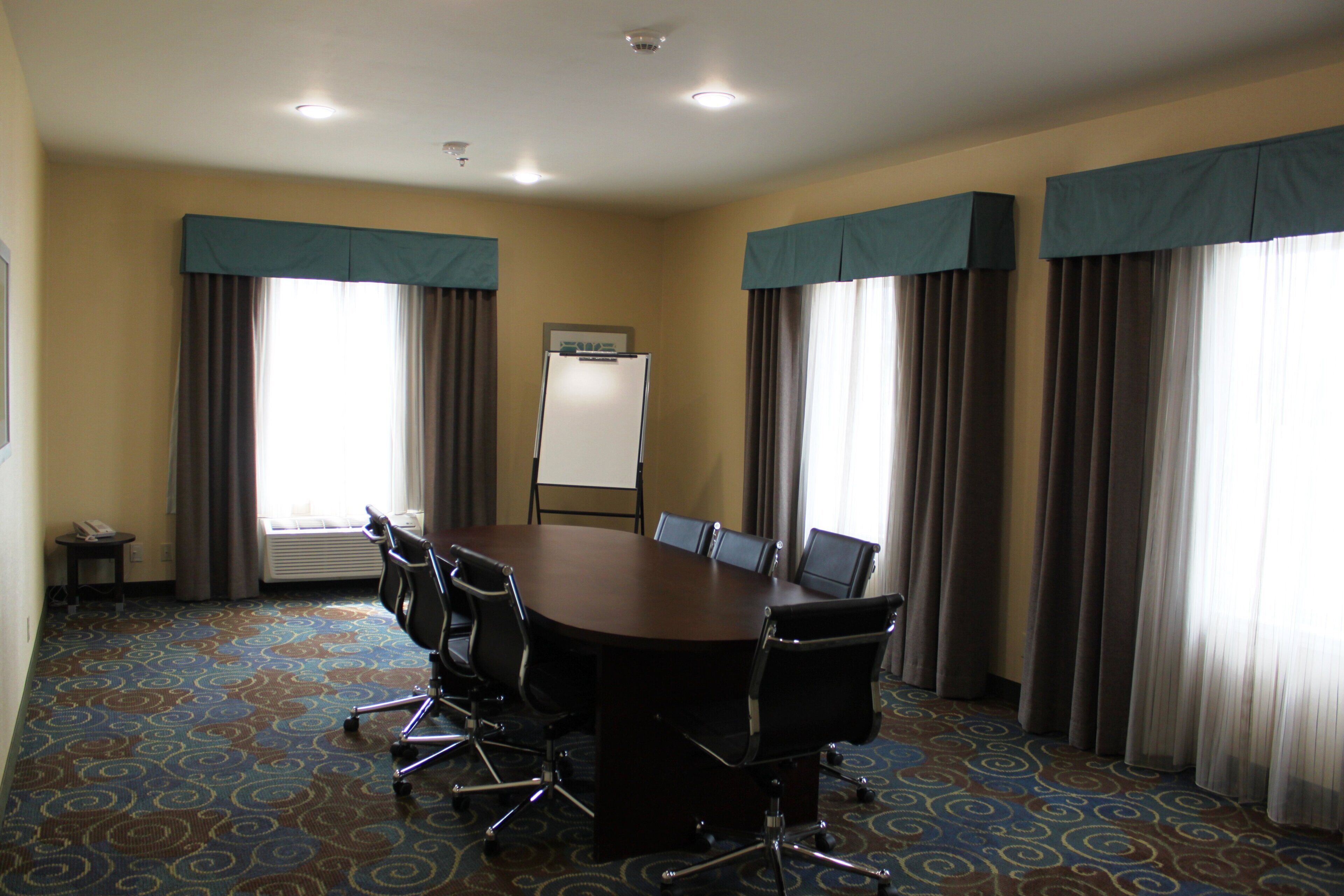 A conference room with a large table, chairs, a whiteboard, and curtains.