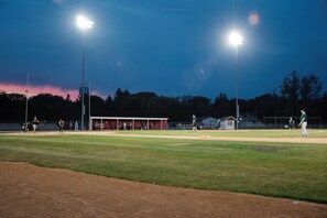 Un terrain de baseball au crépuscule, éclairé par des projecteurs, avec un banc pour les joueurs et des joueurs présents.