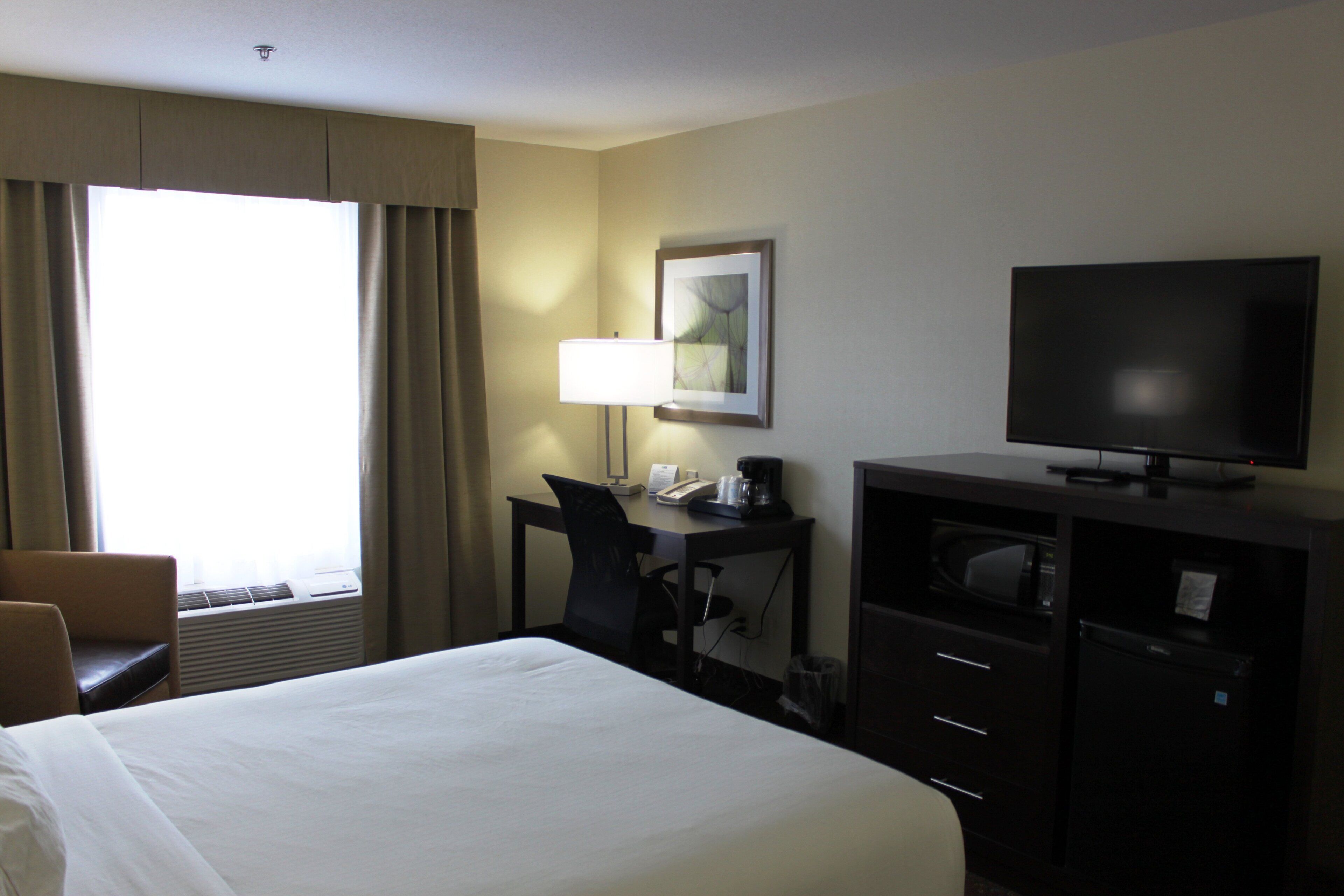 Une chambre d’hôtel équipée d’un lit, d’un bureau, d’une chaise, d’une télévision et d’une fenêtre avec des rideaux.