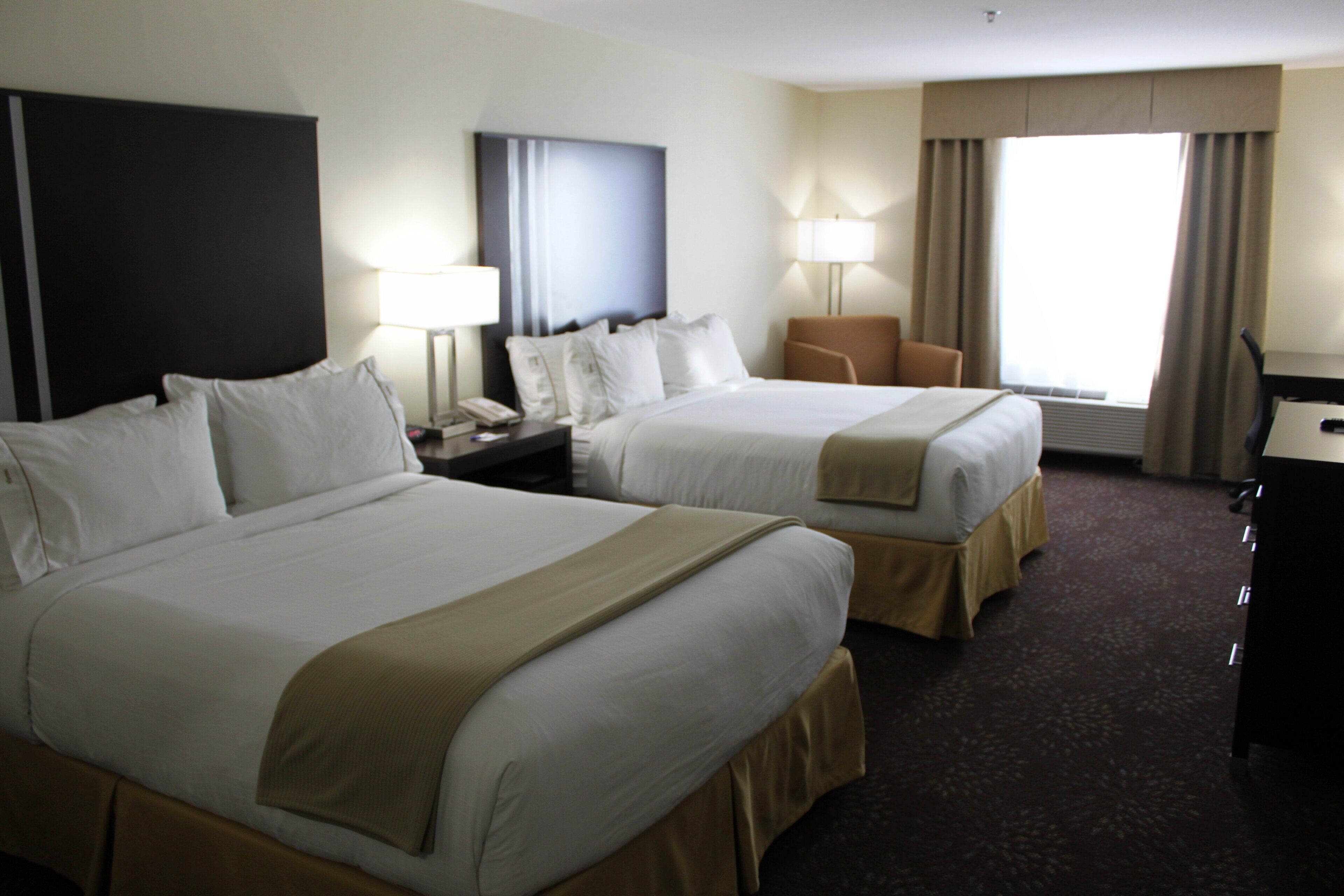 A hotel room with two beds, a desk, a chair, a TV, and a window with curtains.