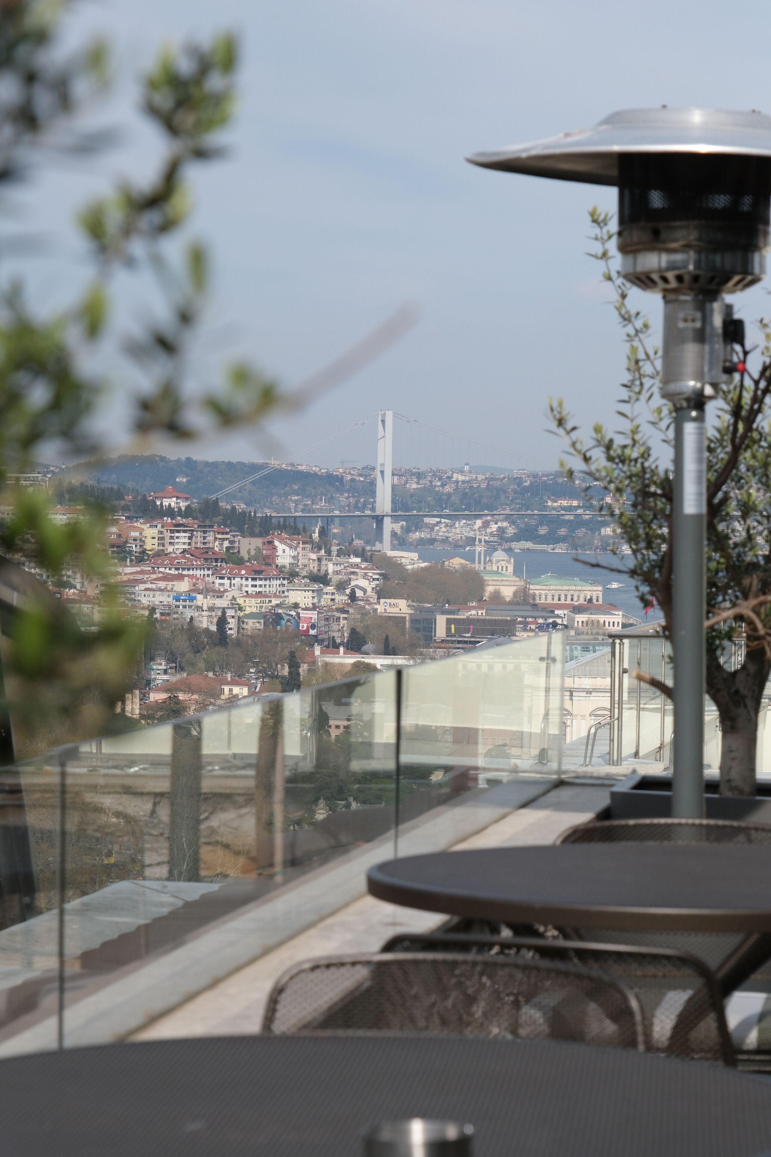 Vista desde un balcón con una mesa y sillas, que da a un paisaje urbano con edificios y un puente.