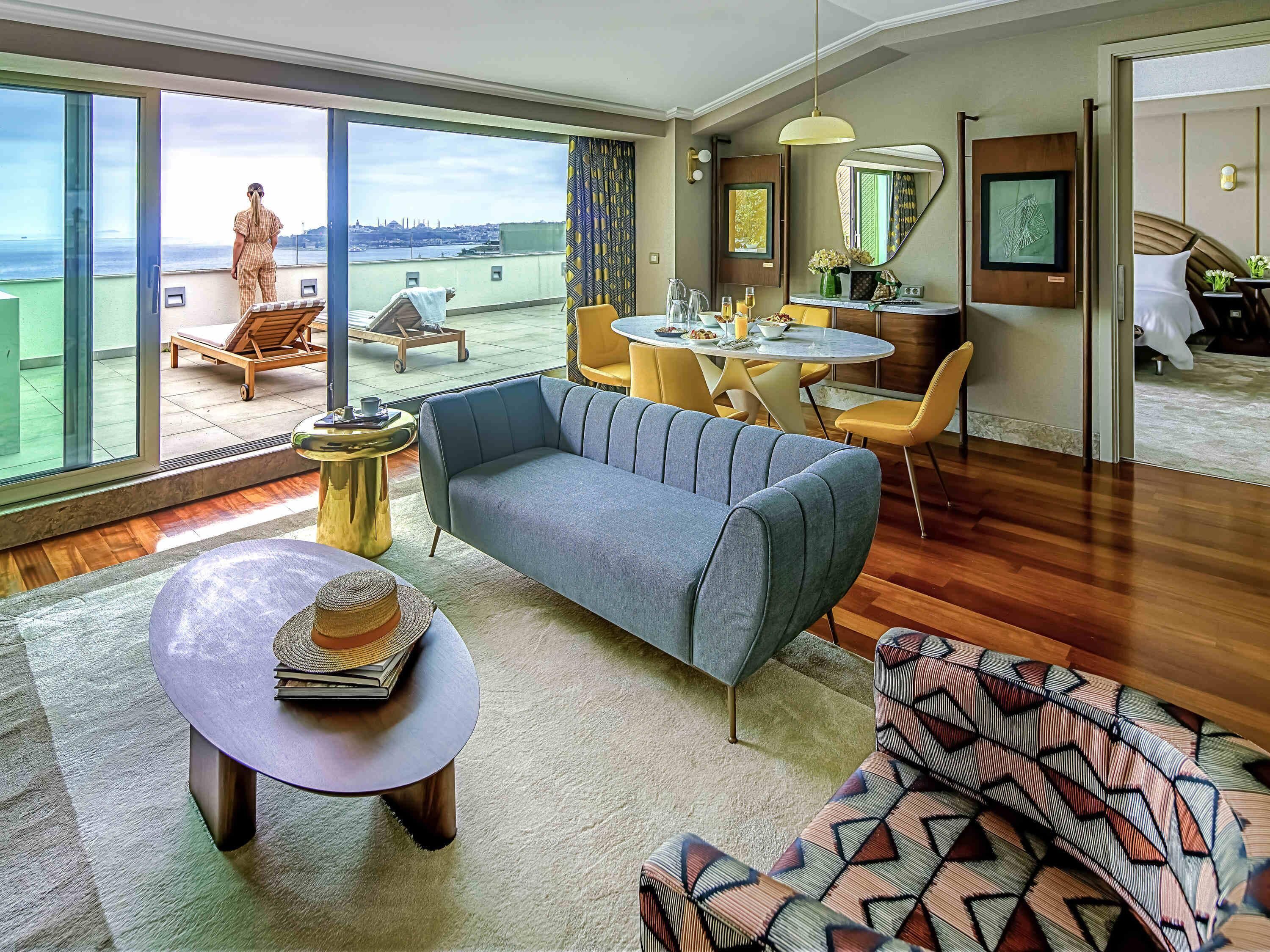Ein modernes Hotelzimmer mit großzügigem Balkon, einem Essbereich und einem Wohnbereich mit Sofa und Couchtisch.