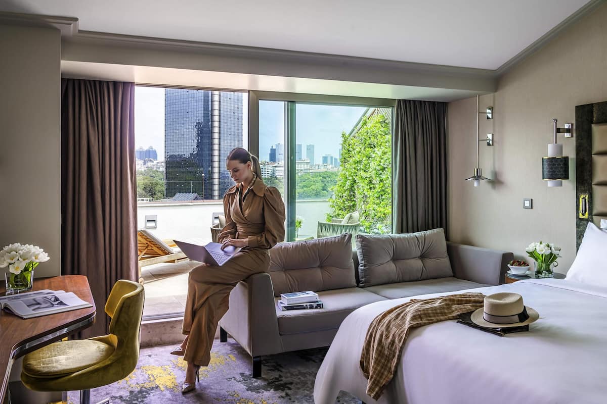 Une chambre d’hôtel comprenant un lit, un canapé, un bureau avec une chaise et une grande fenêtre donnant sur la ville.