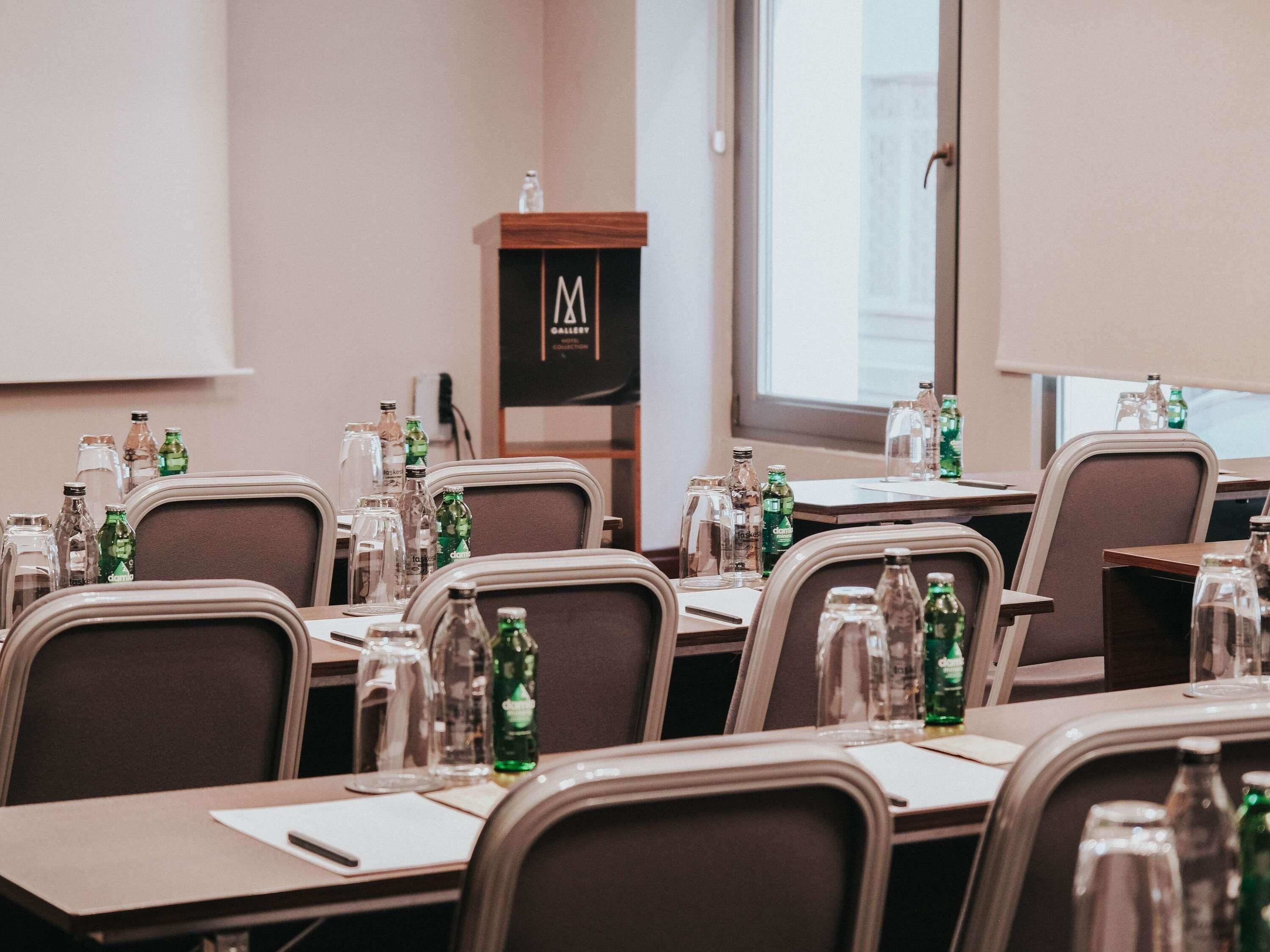 Une salle de conférence équipée de tables, de chaises, de bouteilles d’eau et d’un écran de projection.