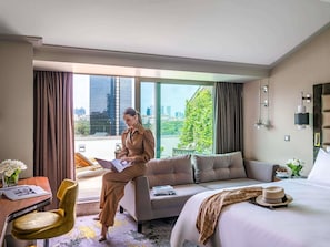 A hotel room with a large window, a sofa, a bed, a desk, and a chair.
