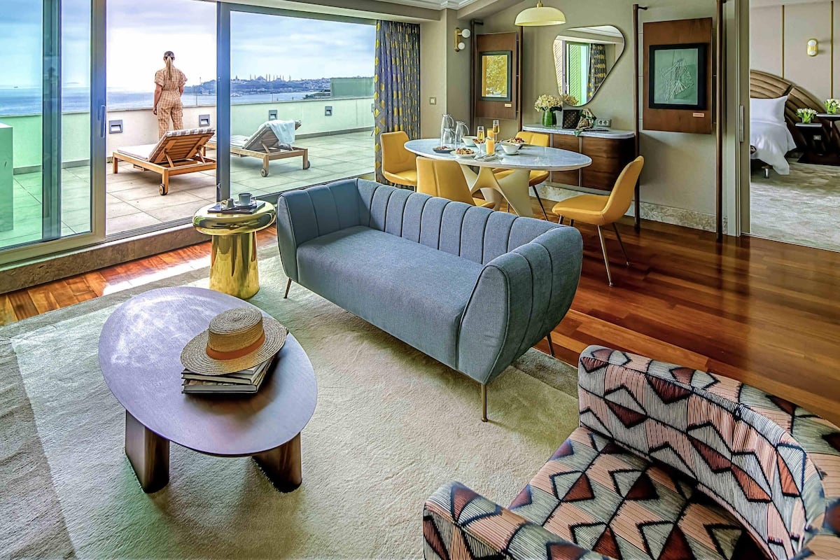 Une chambre d’hôtel moderne dotée d’un grand balcon, d’un coin repas et d’un espace de vie comprenant un canapé et une table basse.
