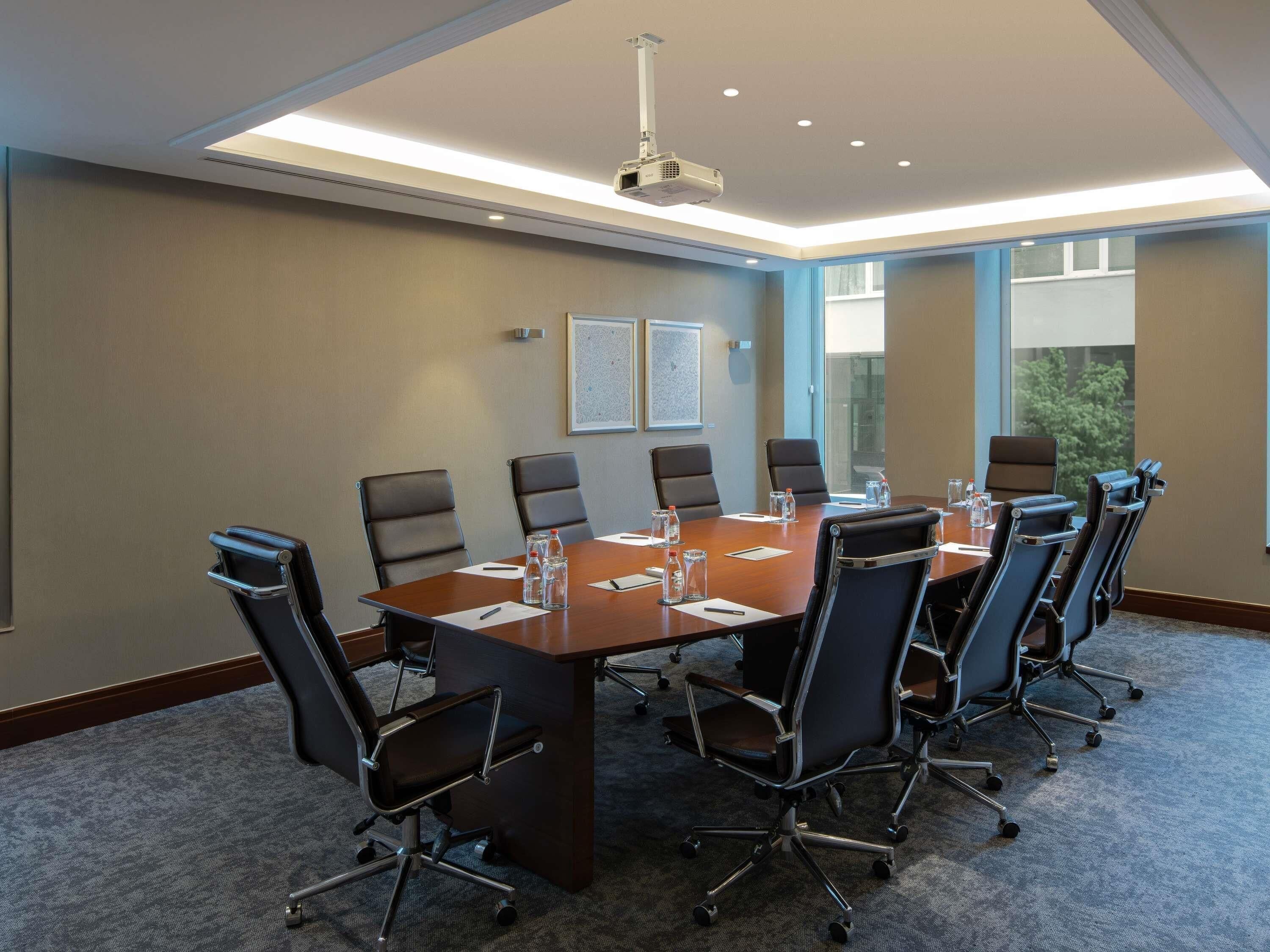 Une salle de conférence avec une longue table, six chaises, un projecteur et une grande fenêtre.