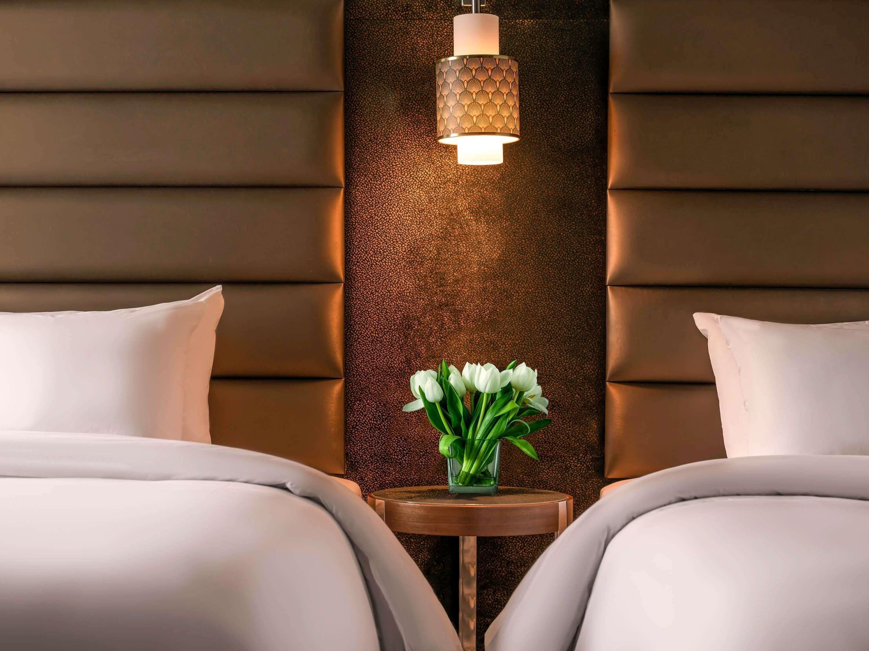 Habitación de hotel con dos camas, un adornado panel decorativo y una pequeña mesa con un florero.