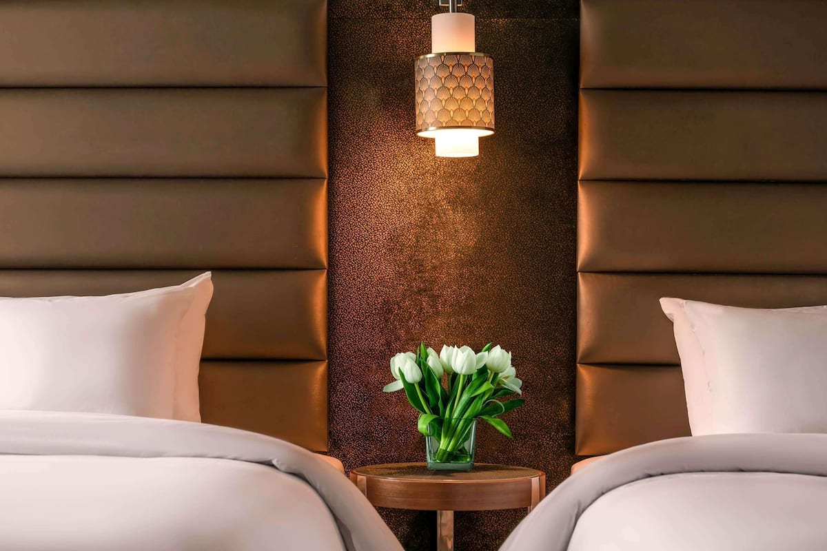 Habitación de hotel con dos camas, un adornado panel decorativo y una pequeña mesa con un florero.