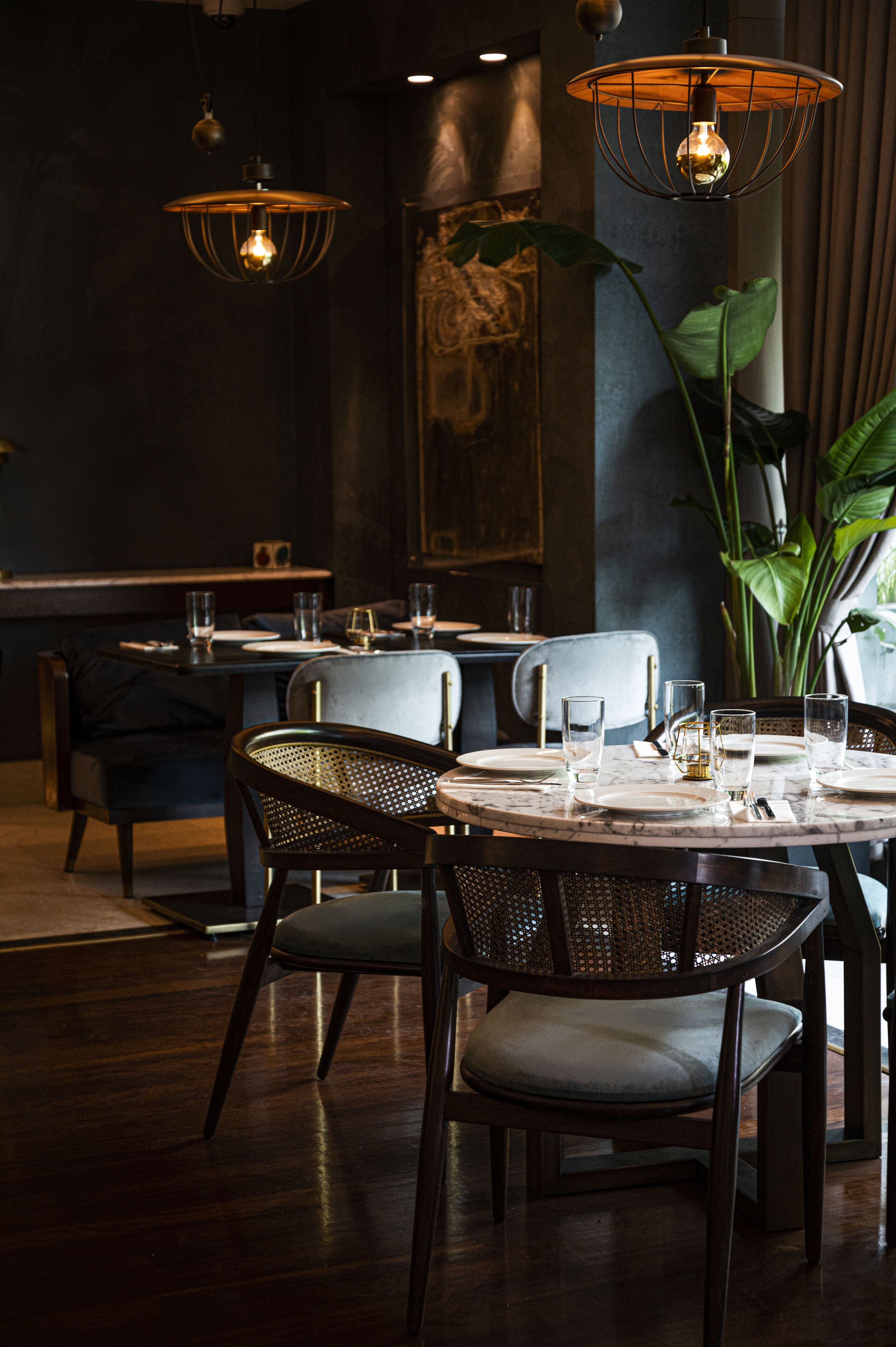 A restaurant interior with round tables, dark wood flooring, and hanging pendant lights.