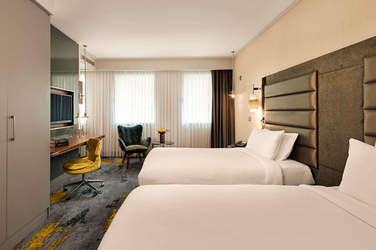 Een hotelkamer met twee bedden, een bureau met stoel, een televisietoestel en een kleine tafel met lamp.