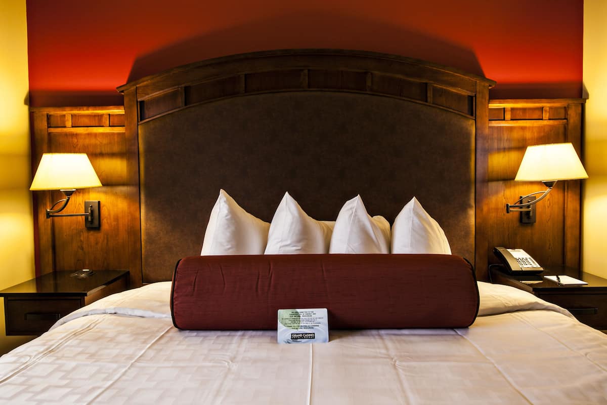 A hotel room with a large bed, a wooden headboard, two bedside tables with lamps, and a telephone.
