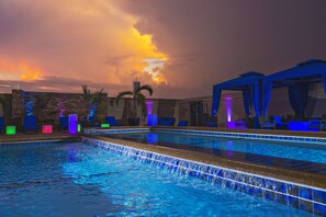 Une piscine agrémentée d’une cascade, de chaises longues et d’un espace salon abrité.