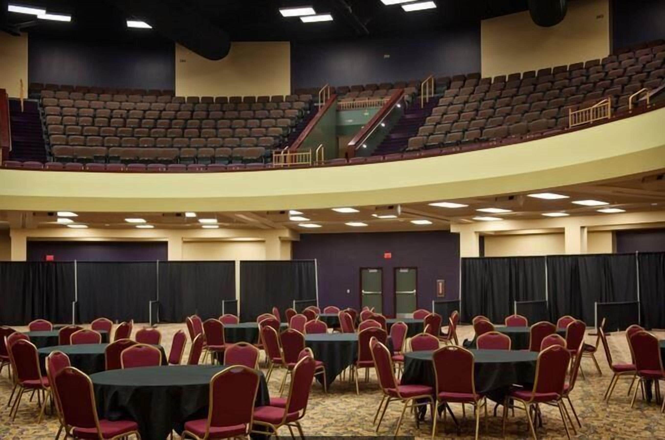 A conference room with tables and chairs, a stage, and a balcony.