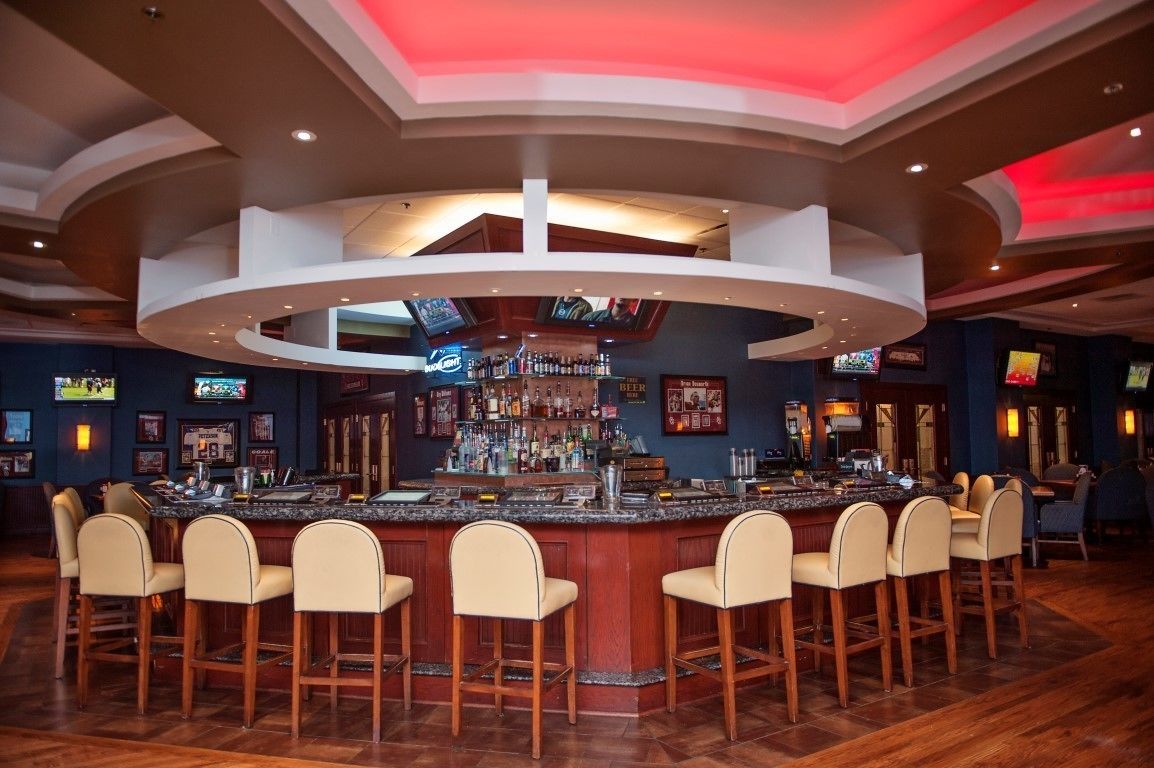 A bar area with a curved counter, multiple stools, and a variety of bottles and glasses.
