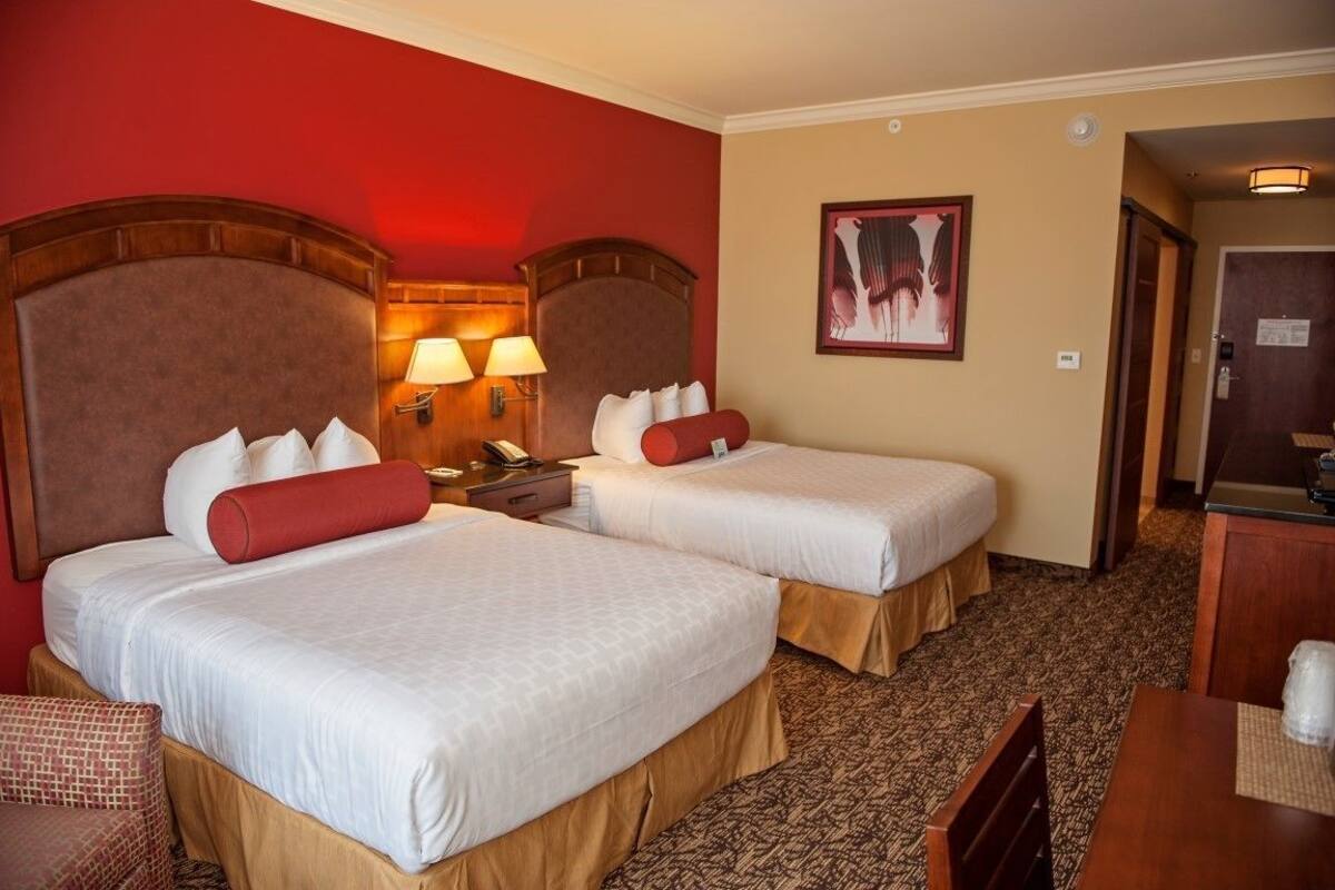 A hotel room with two beds, a desk, a chair, and a painting on the wall.