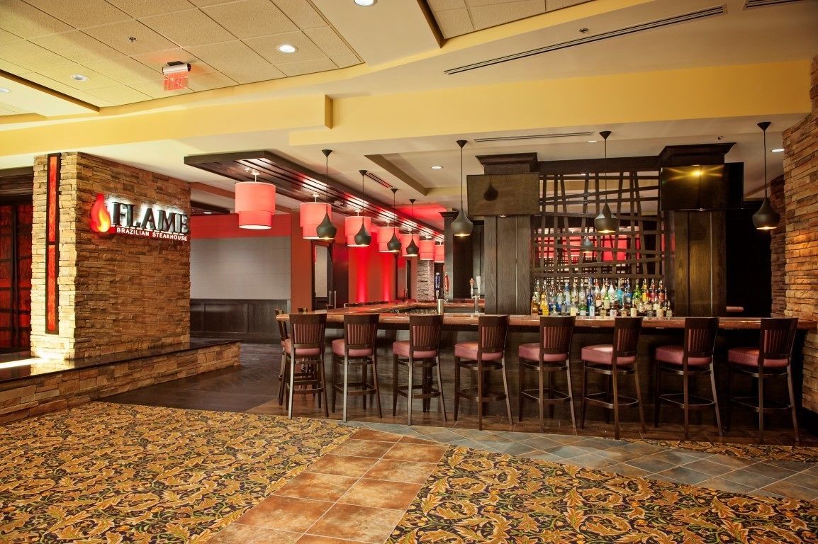 A bar area with a stone wall and a red sign, multiple bar stools, and a patterned carpet.