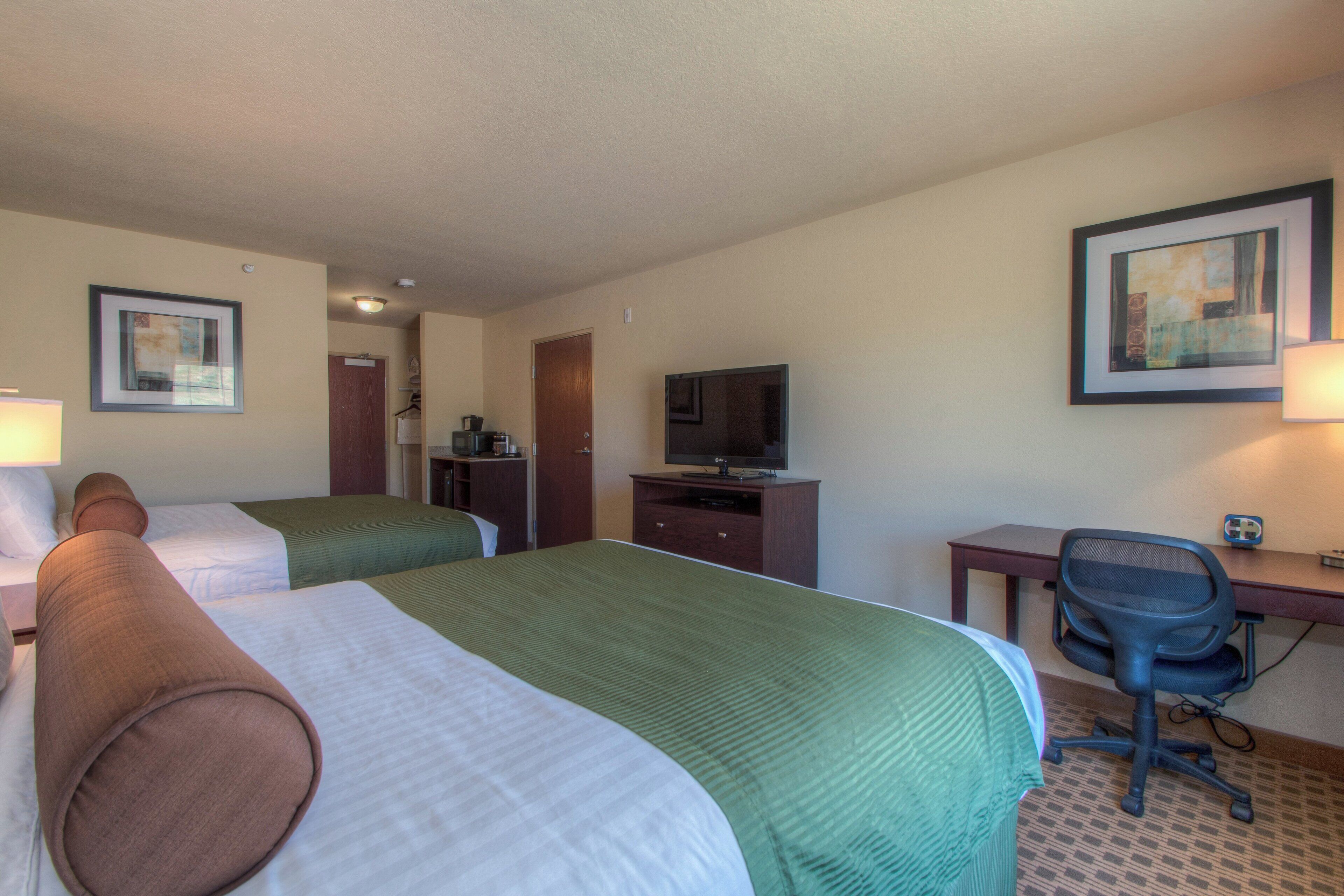 A hotel room with two beds, a desk with a chair, a television, and a framed picture on the wall.