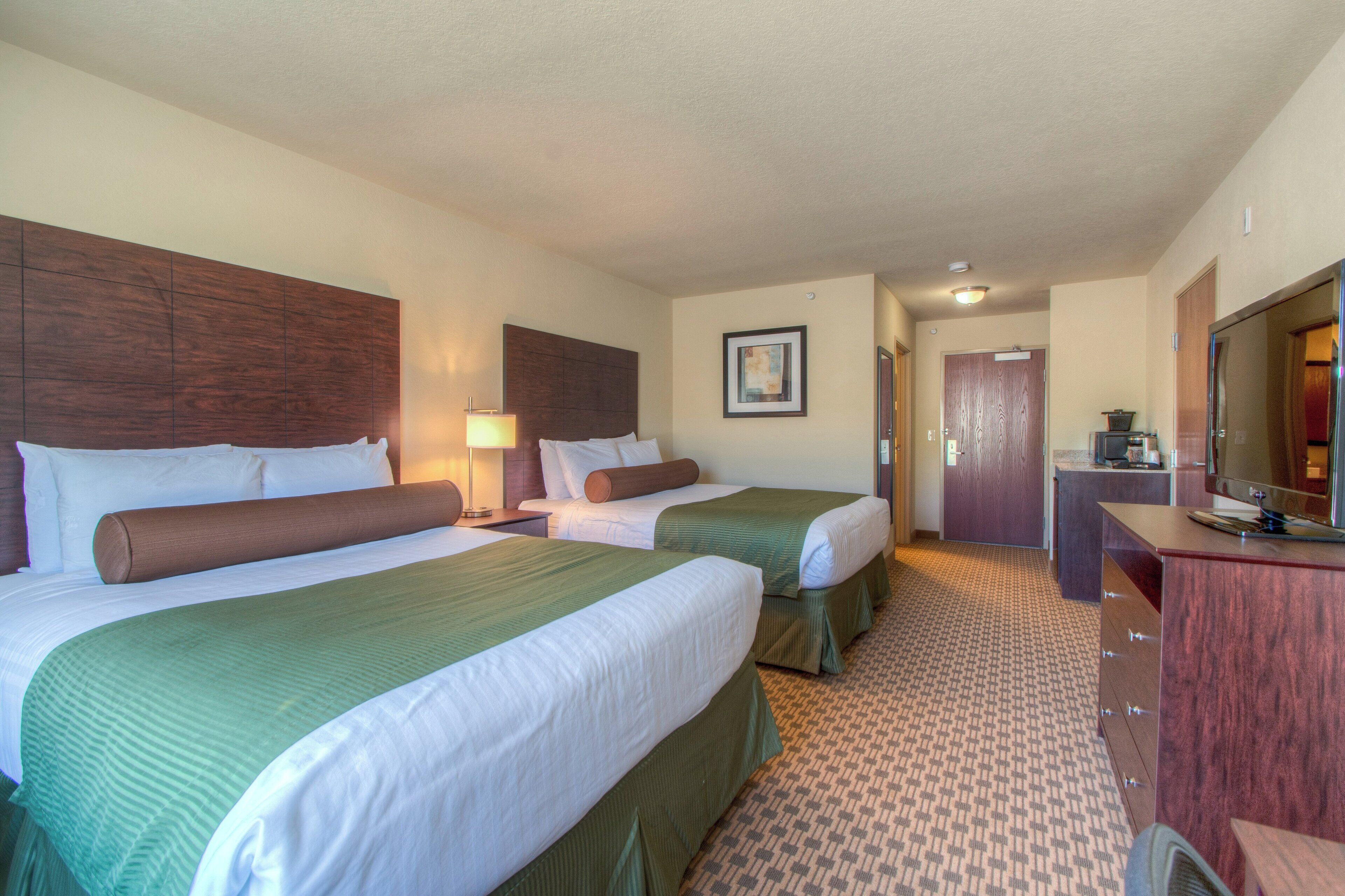 A hotel room with two beds, a desk, a mirror, and a bathroom door.