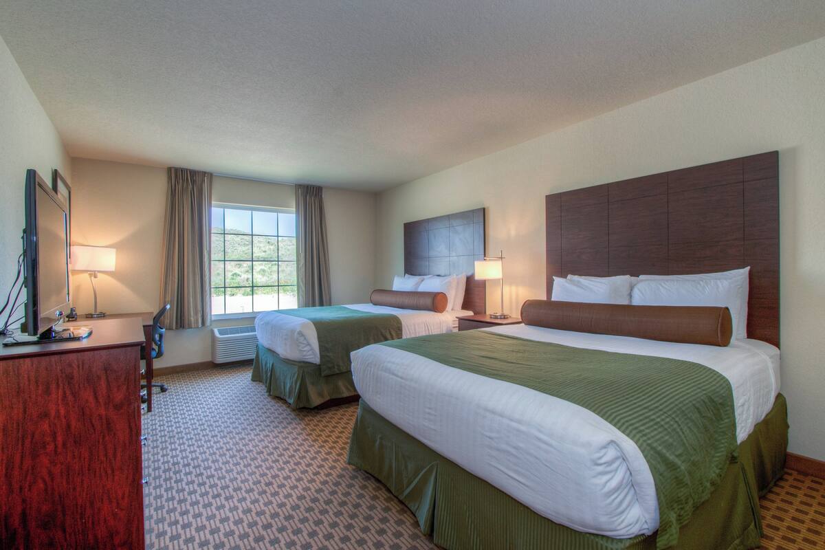 A hotel room with two beds, a desk, a chair, a TV, and a window with curtains.