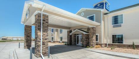 A hotel with a covered entrance, stone pillars, and a sign indicating it is a Cobblestone Inn & Suites.