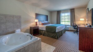 Habitación de hotel con una bañera grande, una cama con cabecera, un escritorio, una silla y una ventana con cortinas.
