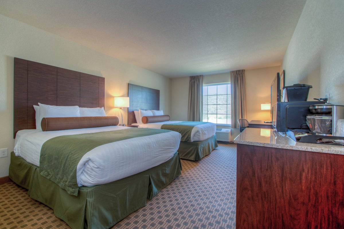 A hotel room with two beds, a desk, a TV, and a window with curtains.