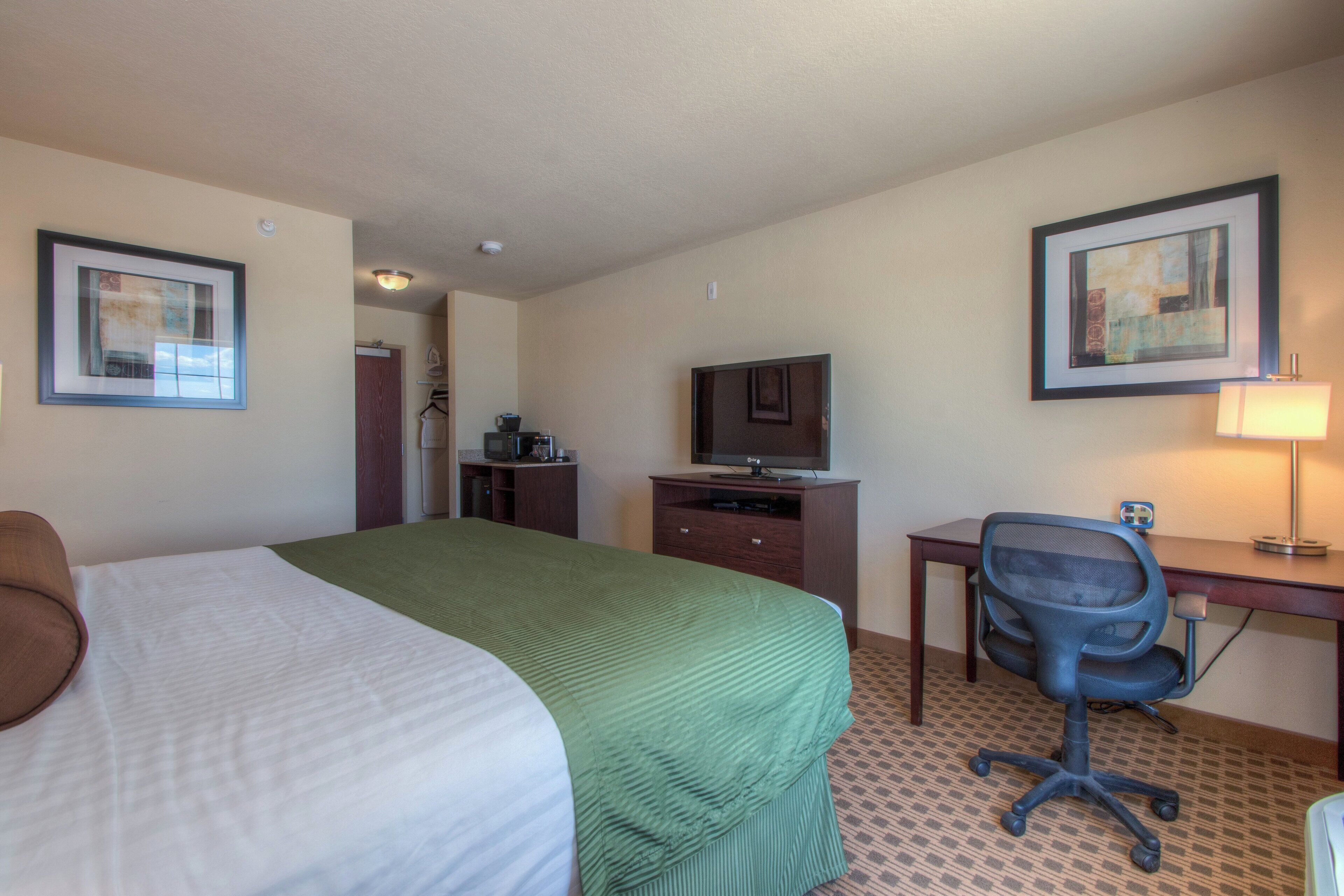 A hotel room with a bed, a desk, a chair, a television, and framed artwork on the walls.