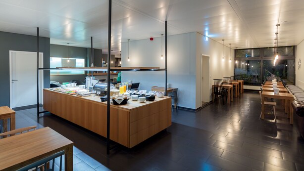 A modern kitchen area with a central island, wooden tables, and a seating area with chairs. - mk | hotel stuttgart (Stuttgart)